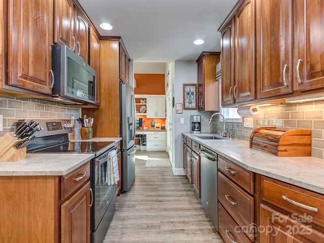 kitchen featuring brown cabinetry, light wood finished floors, a sink, light countertops, and appliances with stainless steel finishes