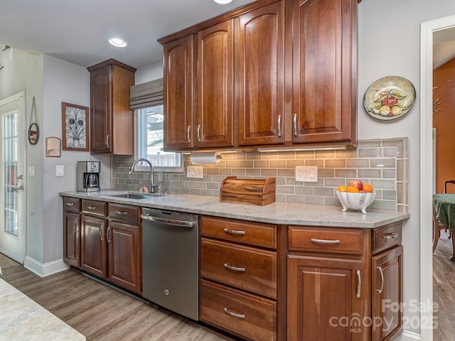 kitchen with backsplash, light stone countertops, light wood-type flooring, stainless steel dishwasher, and a sink