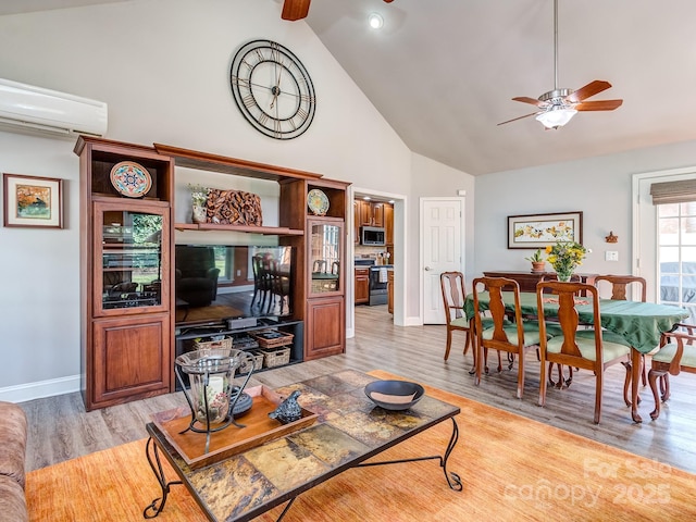 living area with light wood finished floors, baseboards, high vaulted ceiling, a wall mounted AC, and a ceiling fan