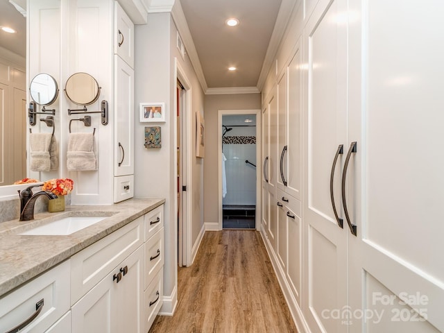 hall featuring a sink, recessed lighting, crown molding, light wood finished floors, and baseboards