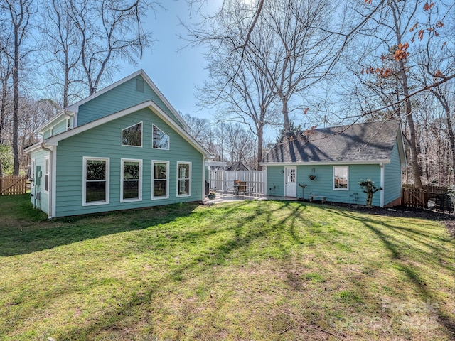 rear view of house featuring a yard, an outbuilding, a shingled roof, and fence