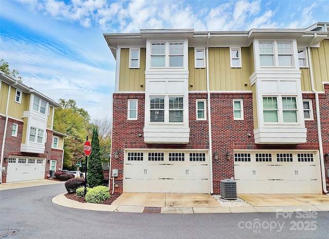 townhome / multi-family property featuring central air condition unit, a garage, brick siding, and driveway