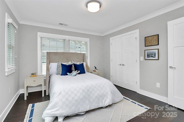 bedroom with visible vents, dark wood-type flooring, ornamental molding, a closet, and baseboards