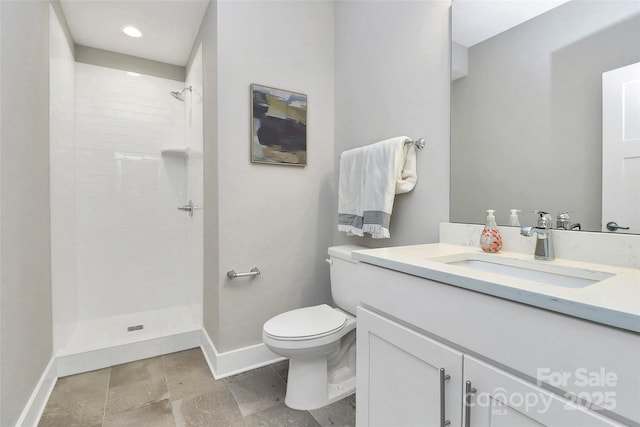 bathroom with tiled shower, toilet, vanity, and baseboards