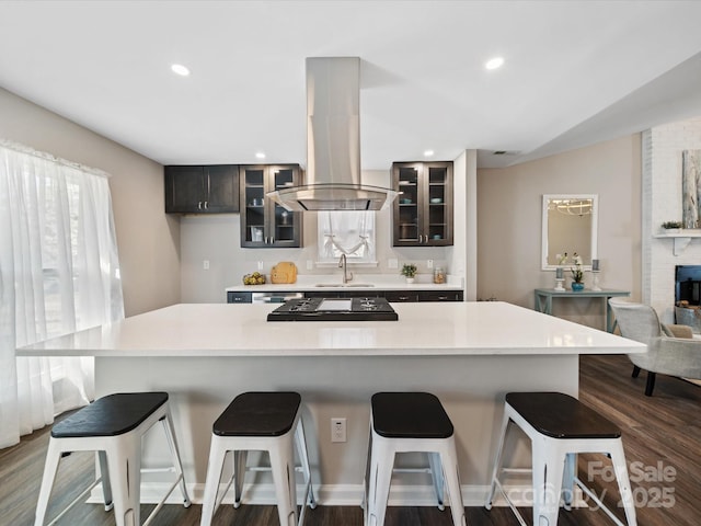 kitchen featuring recessed lighting, a sink, light countertops, glass insert cabinets, and island range hood