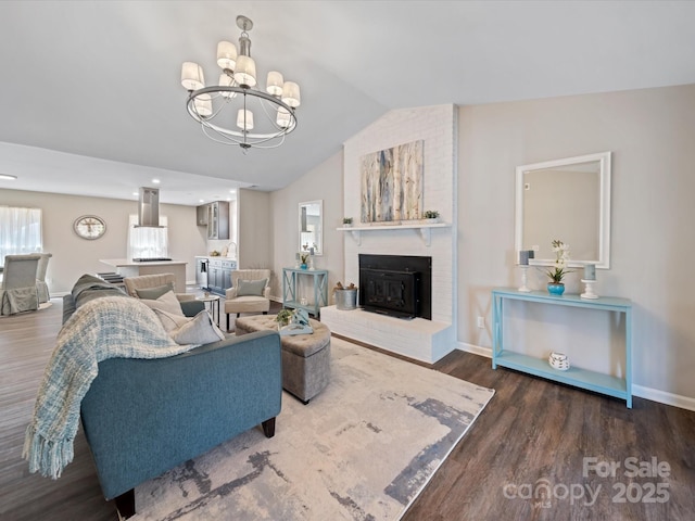 living room featuring baseboards, lofted ceiling, a fireplace, an inviting chandelier, and wood finished floors