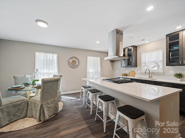 kitchen with a sink, dark wood-type flooring, a kitchen breakfast bar, black gas stovetop, and island range hood