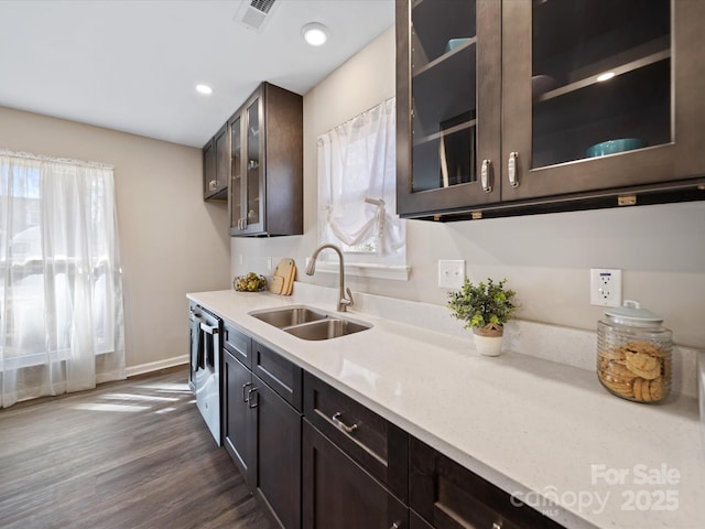 kitchen featuring a sink, glass insert cabinets, dark brown cabinetry, and visible vents