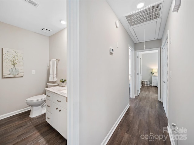 hallway featuring visible vents, baseboards, dark wood-type flooring, and attic access