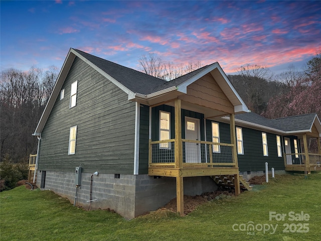 property exterior at dusk with crawl space, a yard, a porch, and roof with shingles