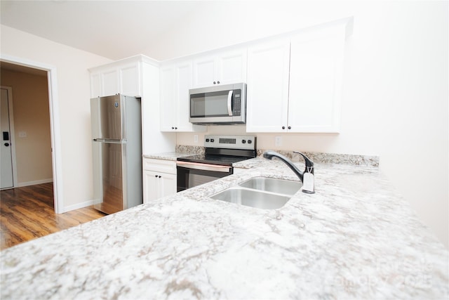 kitchen with light stone counters, wood finished floors, a sink, white cabinets, and appliances with stainless steel finishes