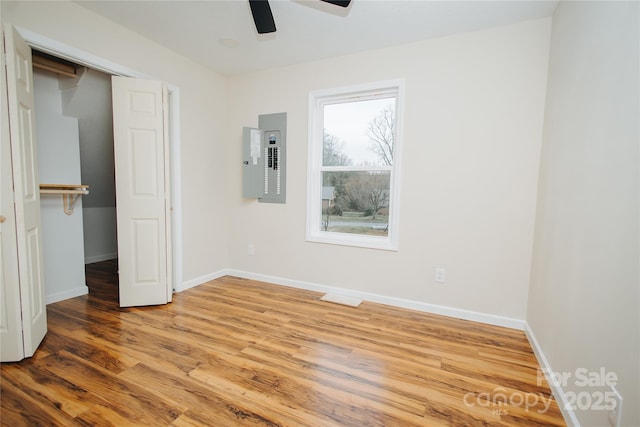 unfurnished bedroom featuring electric panel, a closet, baseboards, and wood finished floors