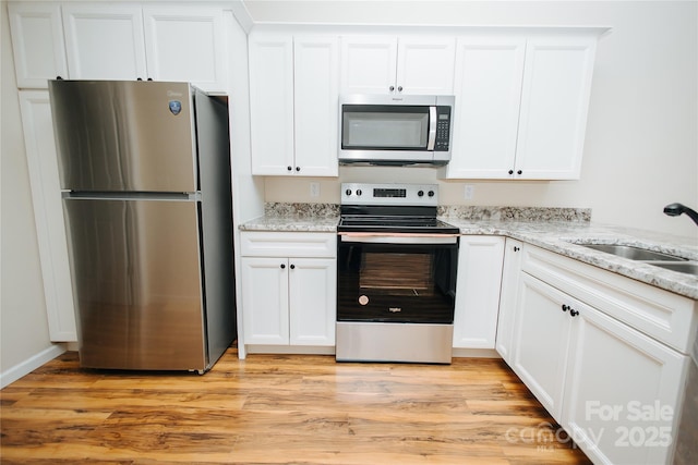 kitchen featuring light stone counters, a sink, stainless steel appliances, white cabinets, and light wood-style floors