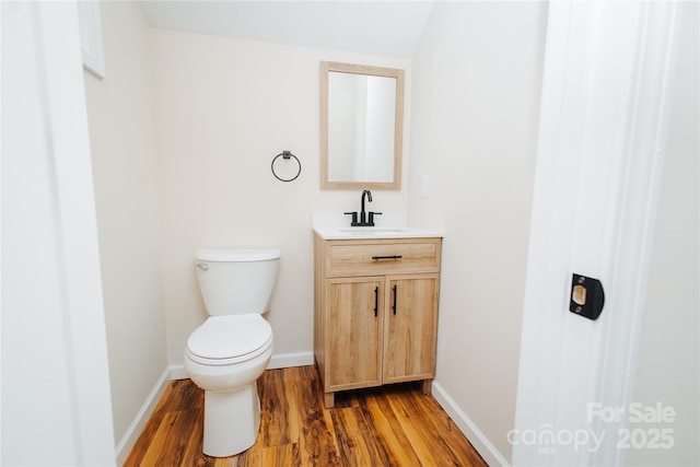 bathroom featuring baseboards, toilet, wood finished floors, and vanity