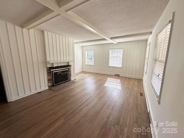 unfurnished living room with beamed ceiling, a fireplace with flush hearth, a textured ceiling, and dark wood-style floors