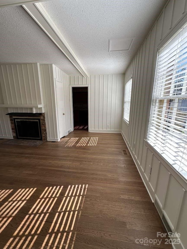 unfurnished living room with visible vents, a brick fireplace, wood finished floors, a decorative wall, and a textured ceiling