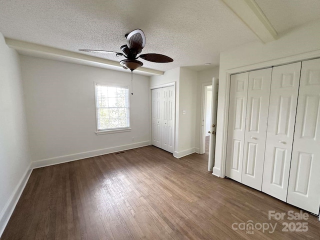 unfurnished bedroom featuring visible vents, two closets, a textured ceiling, baseboards, and dark wood-style flooring