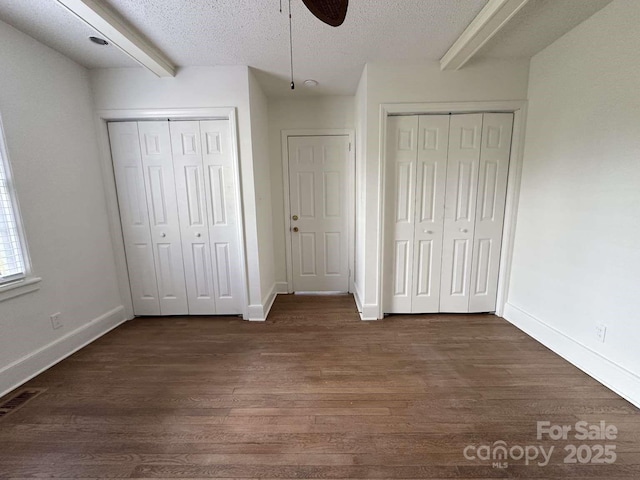 unfurnished bedroom with multiple closets, dark wood-type flooring, beam ceiling, and a textured ceiling