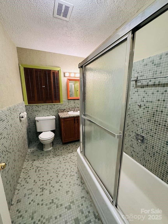 full bath featuring visible vents, toilet, a textured ceiling, and tile walls