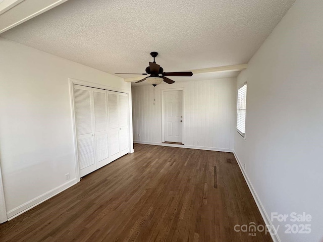 unfurnished bedroom featuring baseboards, dark wood-style flooring, a closet, and a textured ceiling