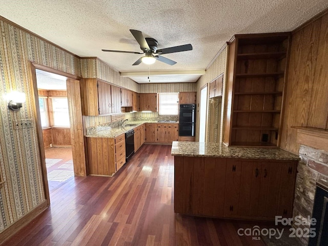 kitchen with wallpapered walls, a peninsula, dark wood-style flooring, black appliances, and brown cabinets