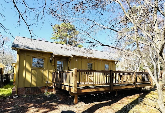 back of house with board and batten siding, a wooden deck, and roof with shingles