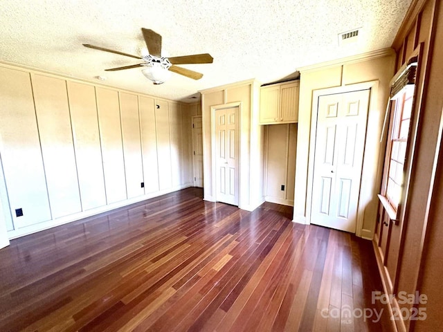 unfurnished bedroom featuring multiple closets, a textured ceiling, dark wood finished floors, crown molding, and ceiling fan