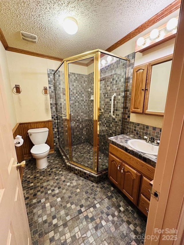 bathroom featuring a textured ceiling, crown molding, toilet, and wainscoting