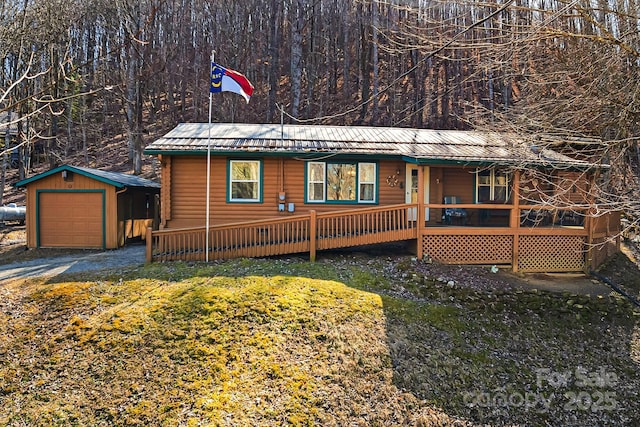 rustic home featuring a detached garage, covered porch, metal roof, an outdoor structure, and driveway