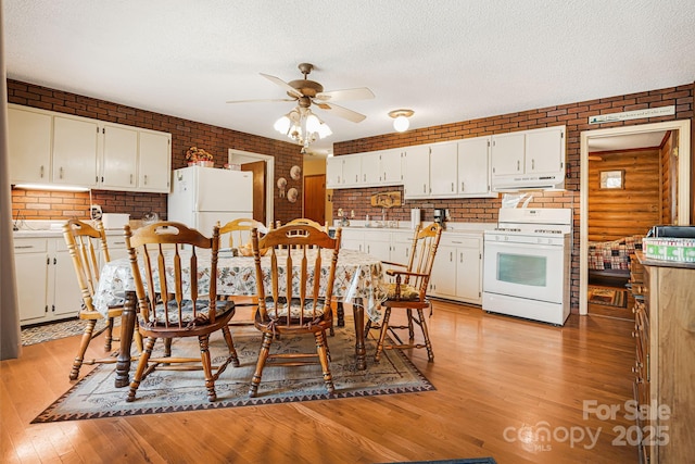 dining area featuring ceiling fan, light wood-style flooring, a textured ceiling, and brick wall