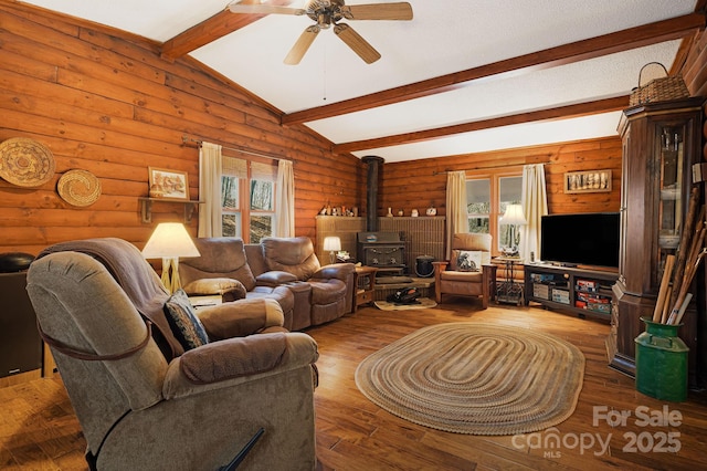 living area featuring hardwood / wood-style floors, lofted ceiling with beams, a wood stove, ceiling fan, and rustic walls