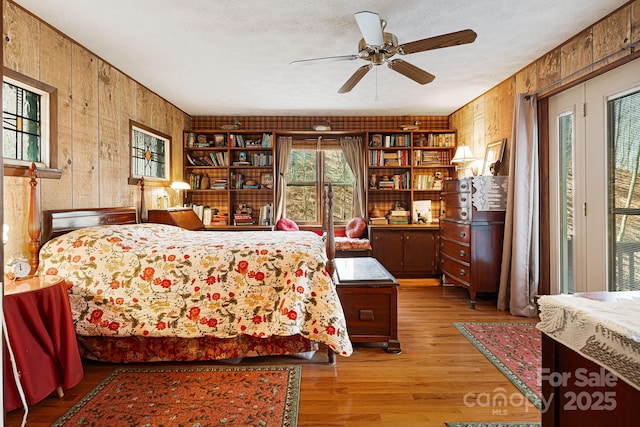 bedroom with wooden walls, a textured ceiling, a ceiling fan, and wood finished floors