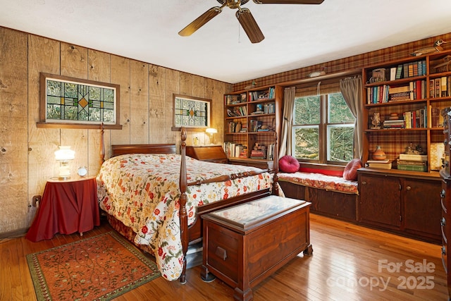 bedroom with wooden walls, a ceiling fan, and hardwood / wood-style flooring