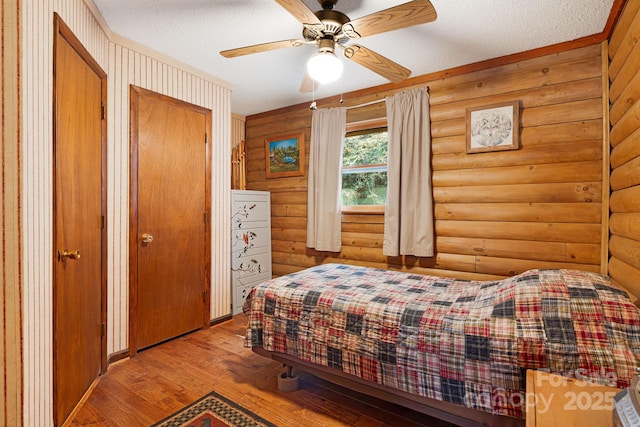 bedroom with ceiling fan, log walls, wood-type flooring, and a textured ceiling