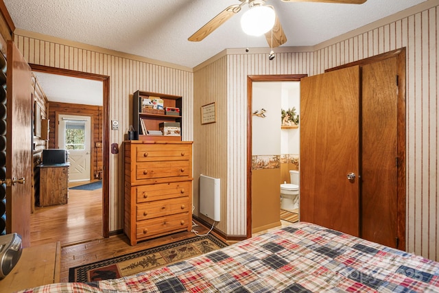 bedroom with wallpapered walls, baseboards, hardwood / wood-style floors, a textured ceiling, and ensuite bath