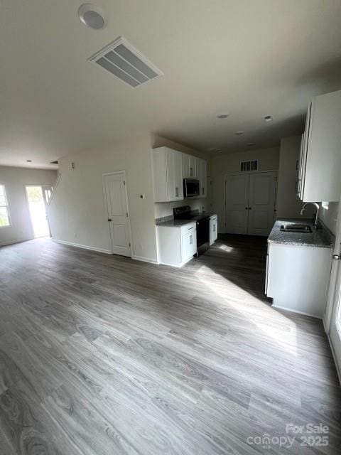 kitchen with stainless steel microwave, range with electric cooktop, open floor plan, white cabinets, and a sink