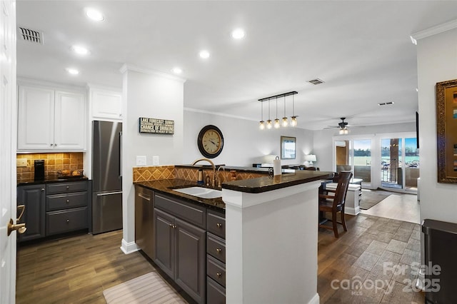 kitchen with dark countertops, visible vents, appliances with stainless steel finishes, a peninsula, and a sink