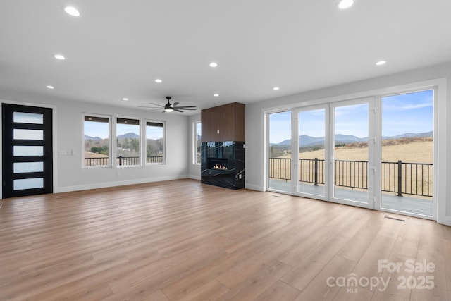 unfurnished living room featuring a wealth of natural light, a mountain view, light wood-style flooring, and a fireplace