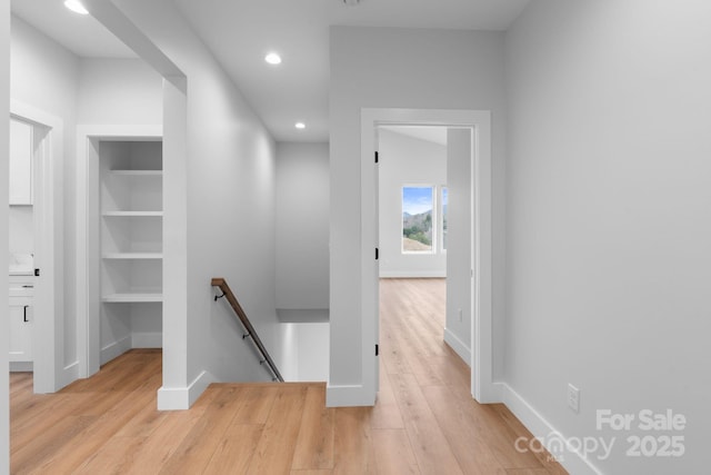 corridor featuring built in shelves, baseboards, recessed lighting, light wood-style floors, and an upstairs landing