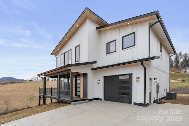 view of front of house with central AC unit, driveway, an attached garage, covered porch, and board and batten siding