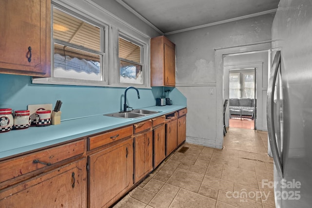 kitchen featuring visible vents, a sink, freestanding refrigerator, brown cabinetry, and light countertops