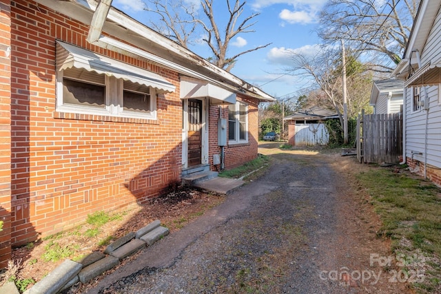 view of side of home featuring brick siding, fence, and dirt driveway