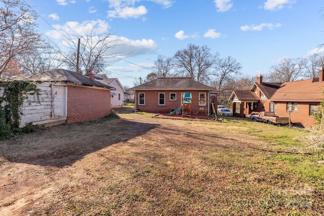 rear view of house featuring brick siding, an outdoor structure, and a lawn