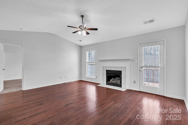 unfurnished living room featuring visible vents, ceiling fan, lofted ceiling, a tile fireplace, and wood finished floors