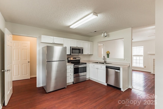 kitchen featuring dark wood-type flooring, light countertops, white cabinets, stainless steel appliances, and a sink