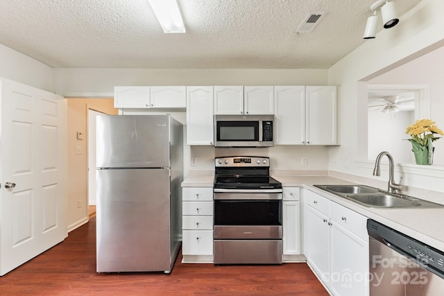 kitchen with a sink, dark wood-style floors, white cabinetry, appliances with stainless steel finishes, and light countertops