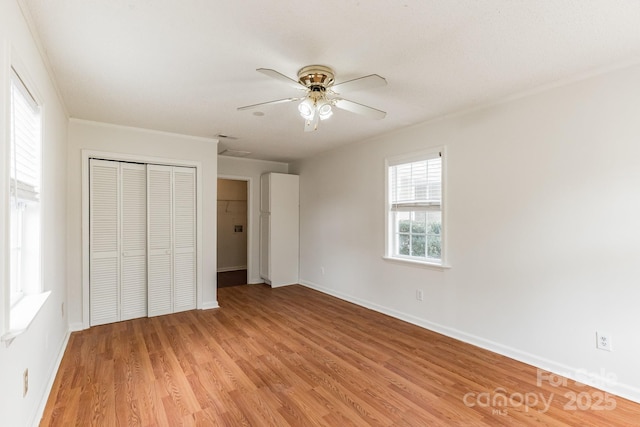 unfurnished bedroom featuring crown molding, baseboards, ceiling fan, light wood-style flooring, and a closet