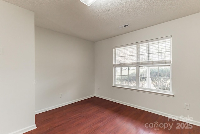 unfurnished room with visible vents, a textured ceiling, baseboards, and wood finished floors