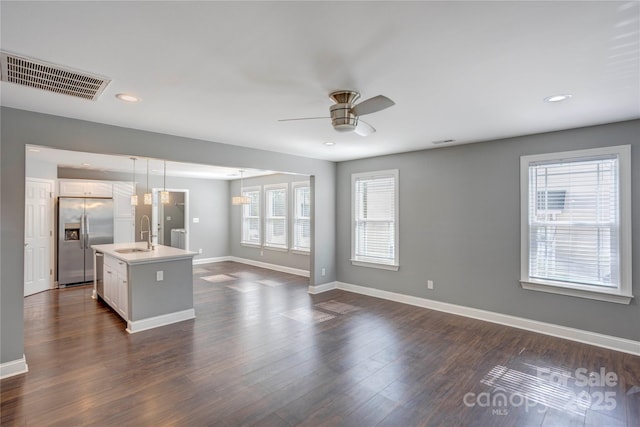 unfurnished living room featuring visible vents, ceiling fan, baseboards, dark wood-style floors, and a sink