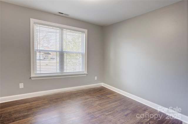 unfurnished room featuring visible vents, baseboards, and dark wood-style floors